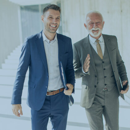 Mature businessman and his young colleague discussing financial Ein älterer und ein jüngerer Geschäftsmann laufen einen Gang entlang und diskutieren.