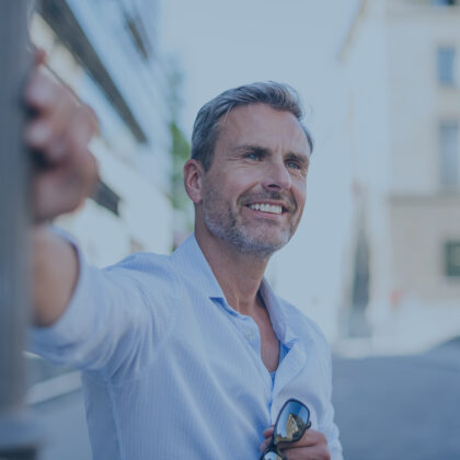 Smiling man leaning against lamp pole in the city Ein sympathischer Mann mittleren Alters lehnt entspannt an einer Laterne und lächelt.